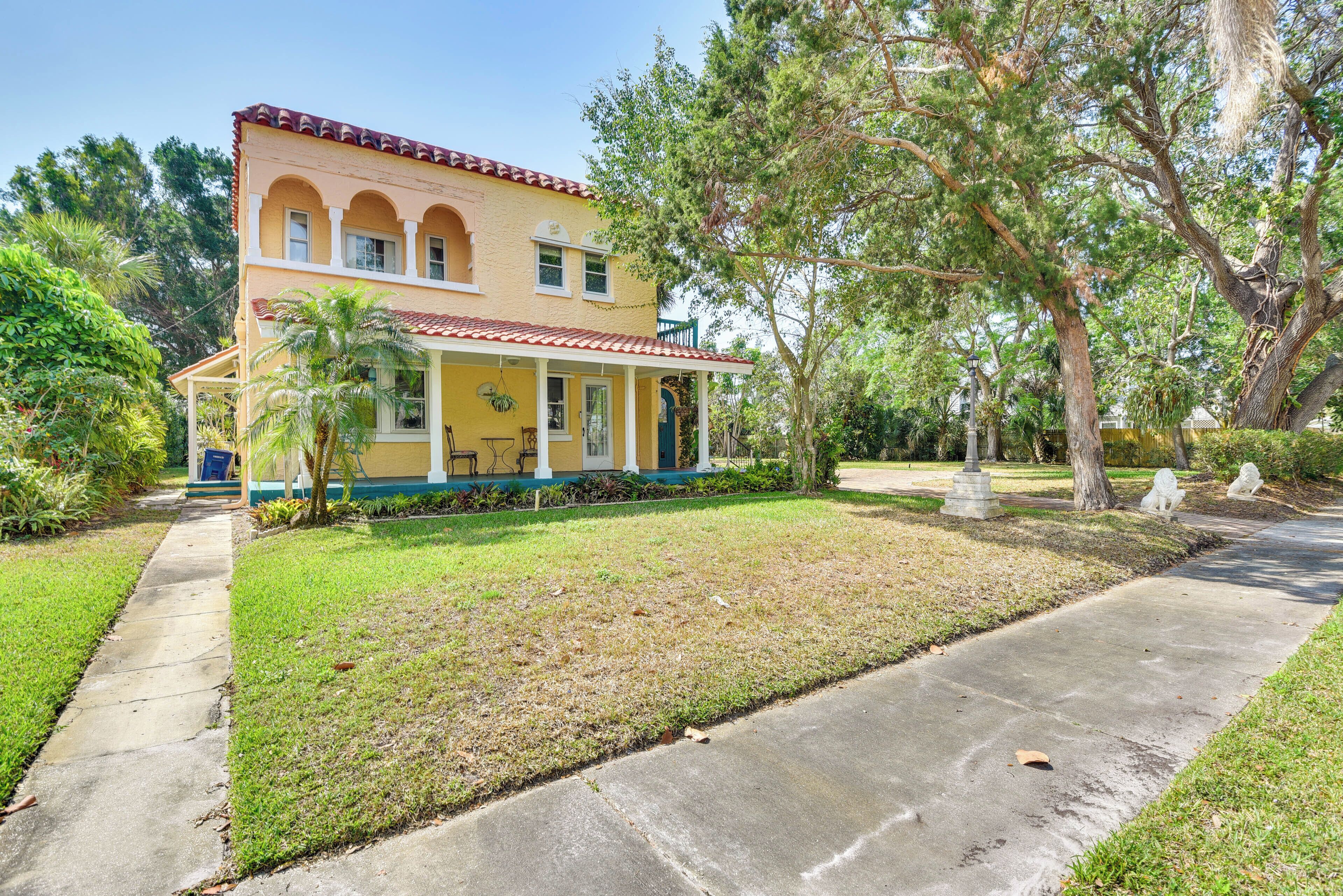 A two-story house with a yellow facade and red-tiled roof, surrounded by a well-maintained lawn and trees.