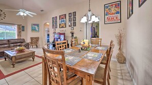 A dining area with a wooden table, chairs, and a chandelier. There are framed pictures on the walls and a ceiling fan. - 10 Mi to Disney + Heated Pool: Florida Abode! (Clermont)