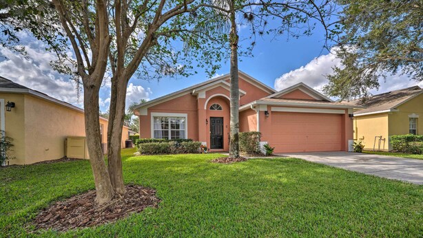 A two-story house with a red garage, a front yard with a tree, and a clear blue sky. - 10 Mi to Disney + Heated Pool: Florida Abode! (Clermont)