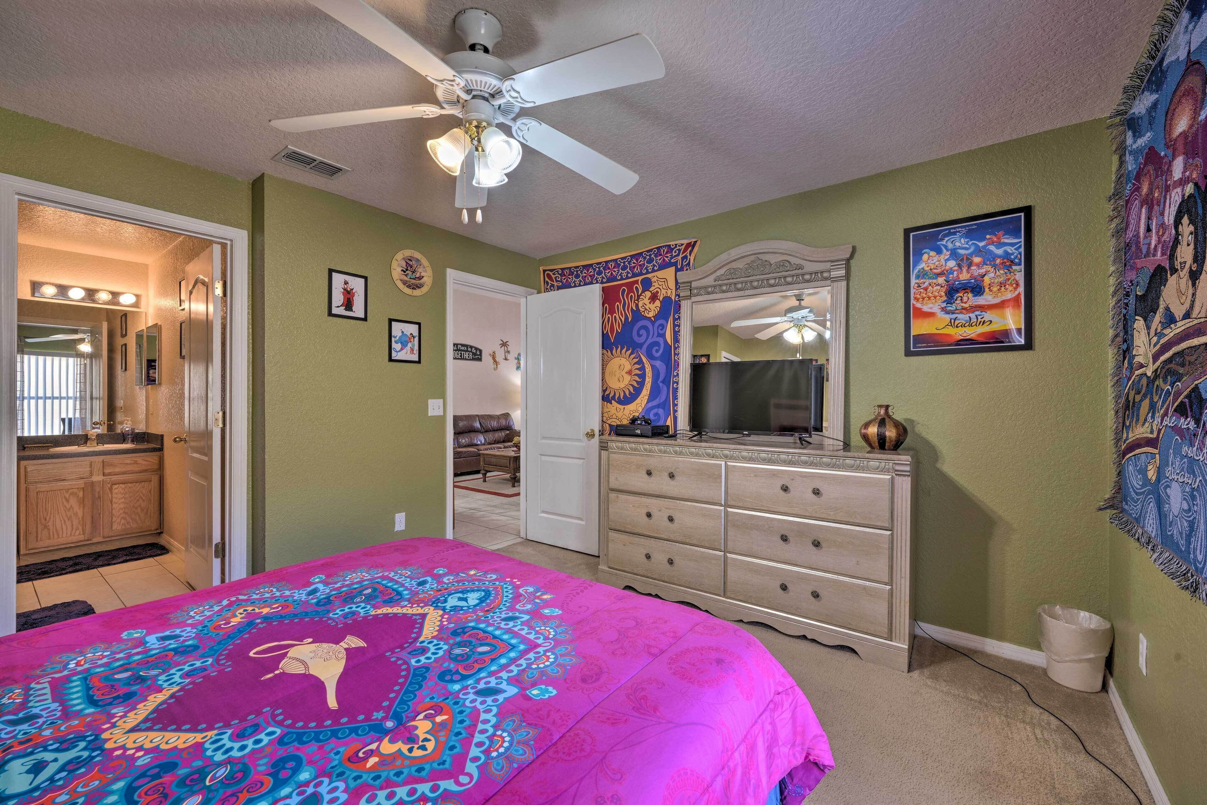 A bedroom with a bed, dresser, ceiling fan, and a door leading to another room.