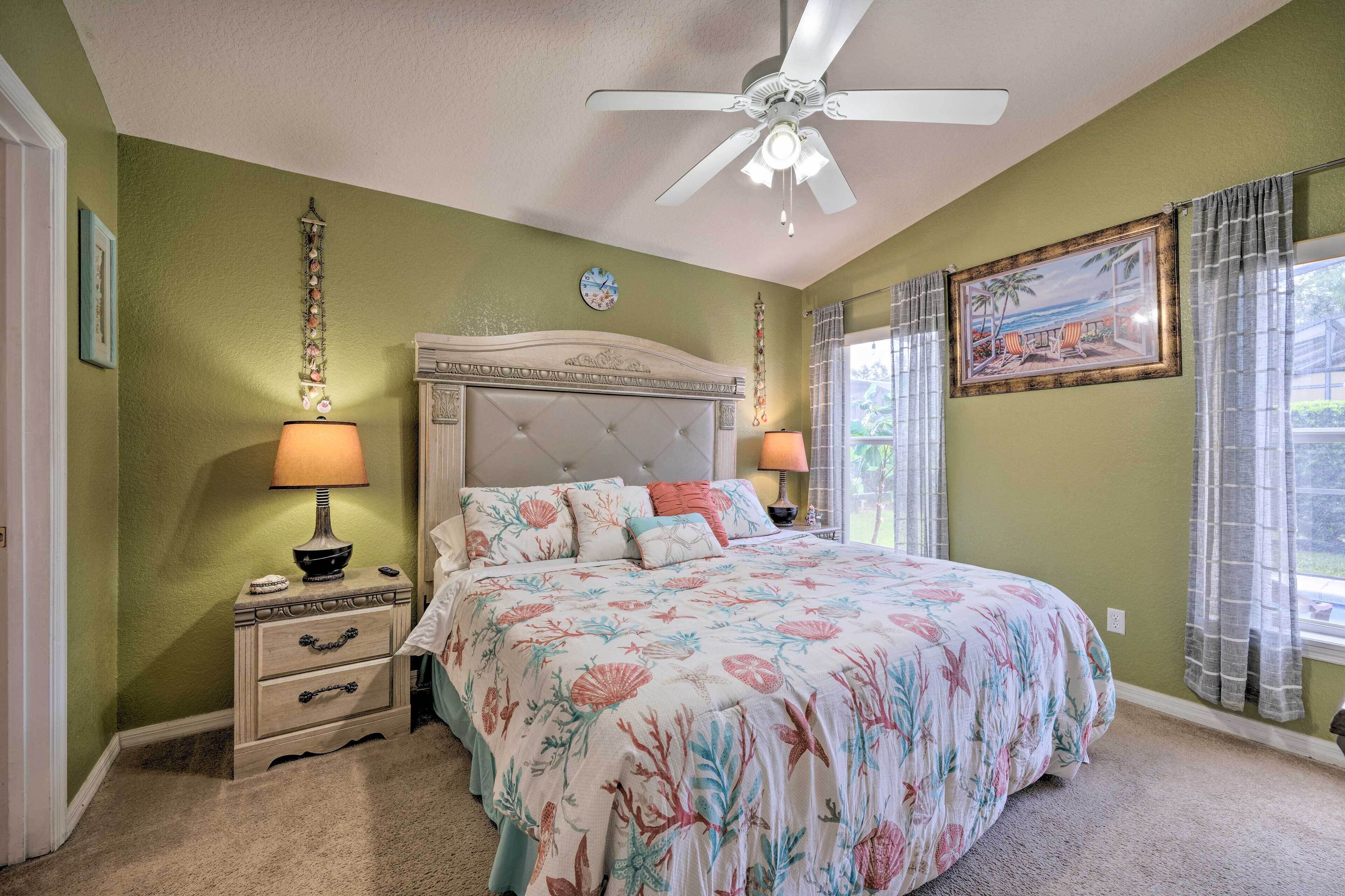 A bedroom with a bed, nightstands, a ceiling fan, a window with curtains, and a wall clock.