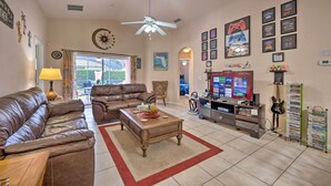 A living room with a brown leather sofa, a wooden coffee table, a ceiling fan, and a TV stand with a guitar and a DVD rack. - 10 Mi to Disney + Heated Pool: Florida Abode! (Clermont)