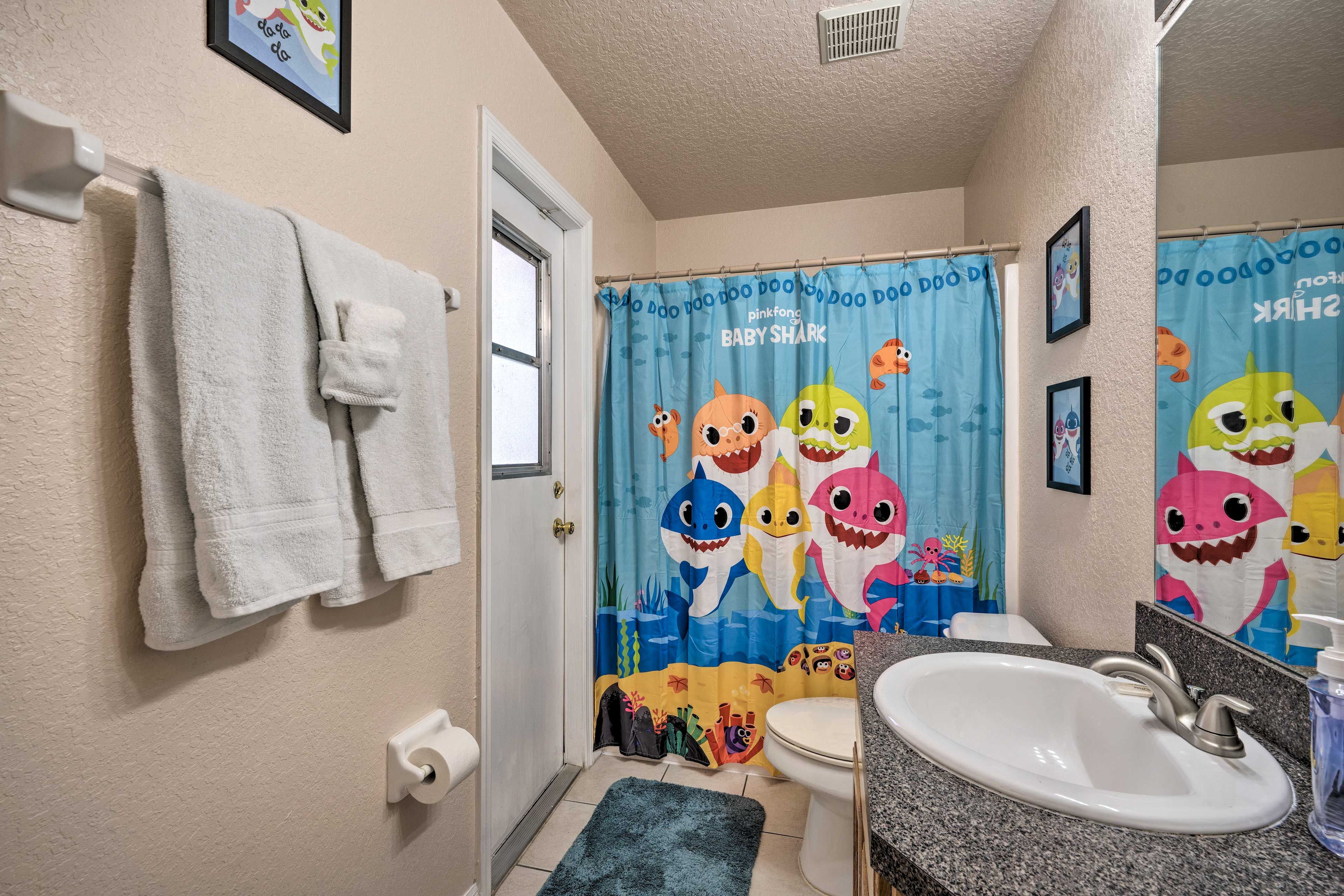 A bathroom with a toilet, sink, and a shower curtain featuring a baby shark theme.