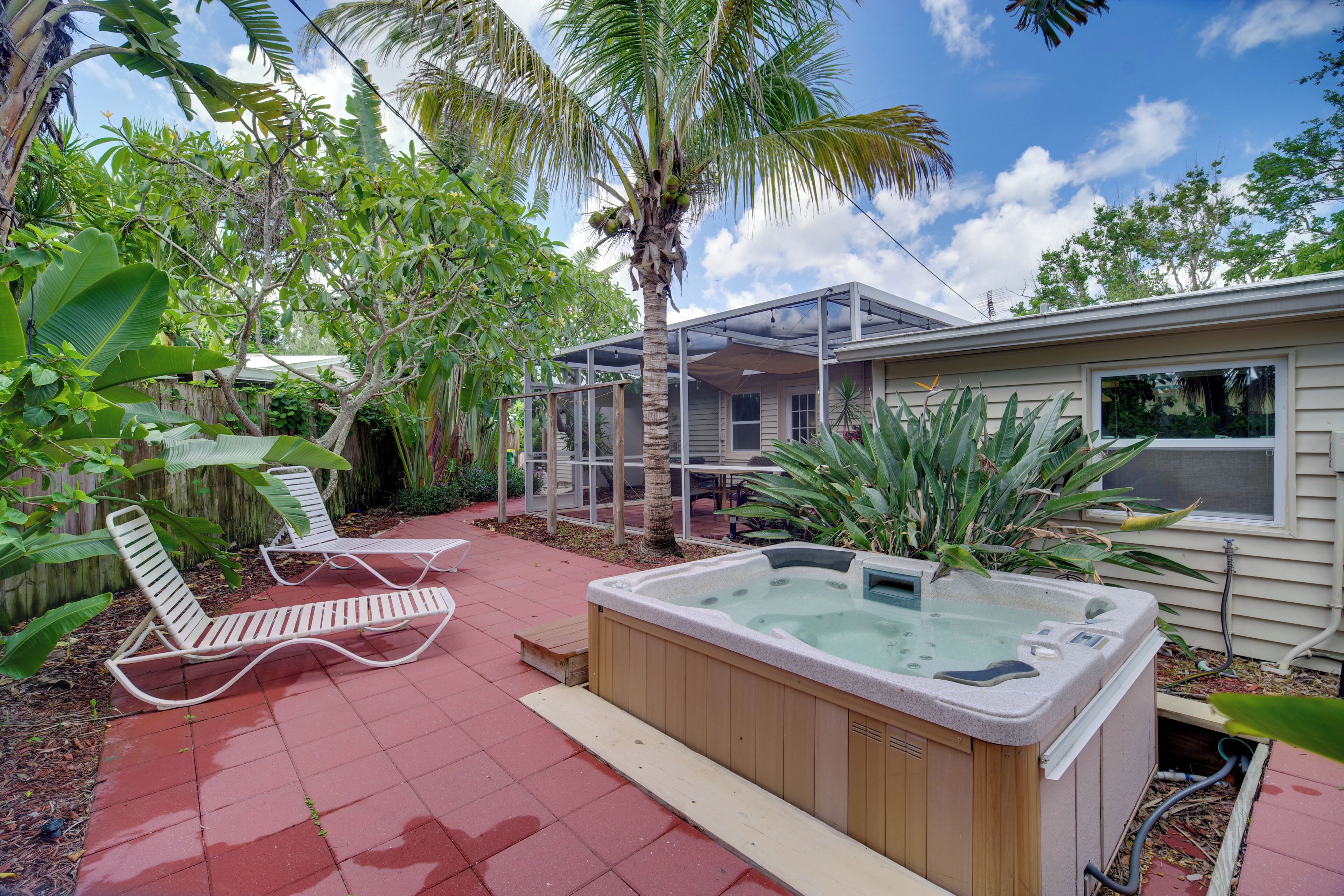 Ein Garten mit Whirlpool, zwei Liegestühlen und einer überdachten Terrasse.