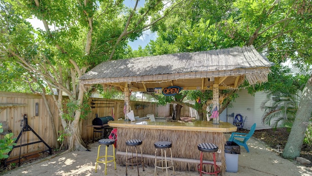 Un espace bar extérieur doté d’un toit de chaume, d’une clôture en bois et de plusieurs tabourets.