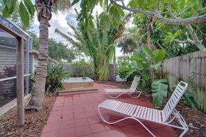 Un patio con dos sillones blancos, un jacuzzi y exuberante vegetación tropical.