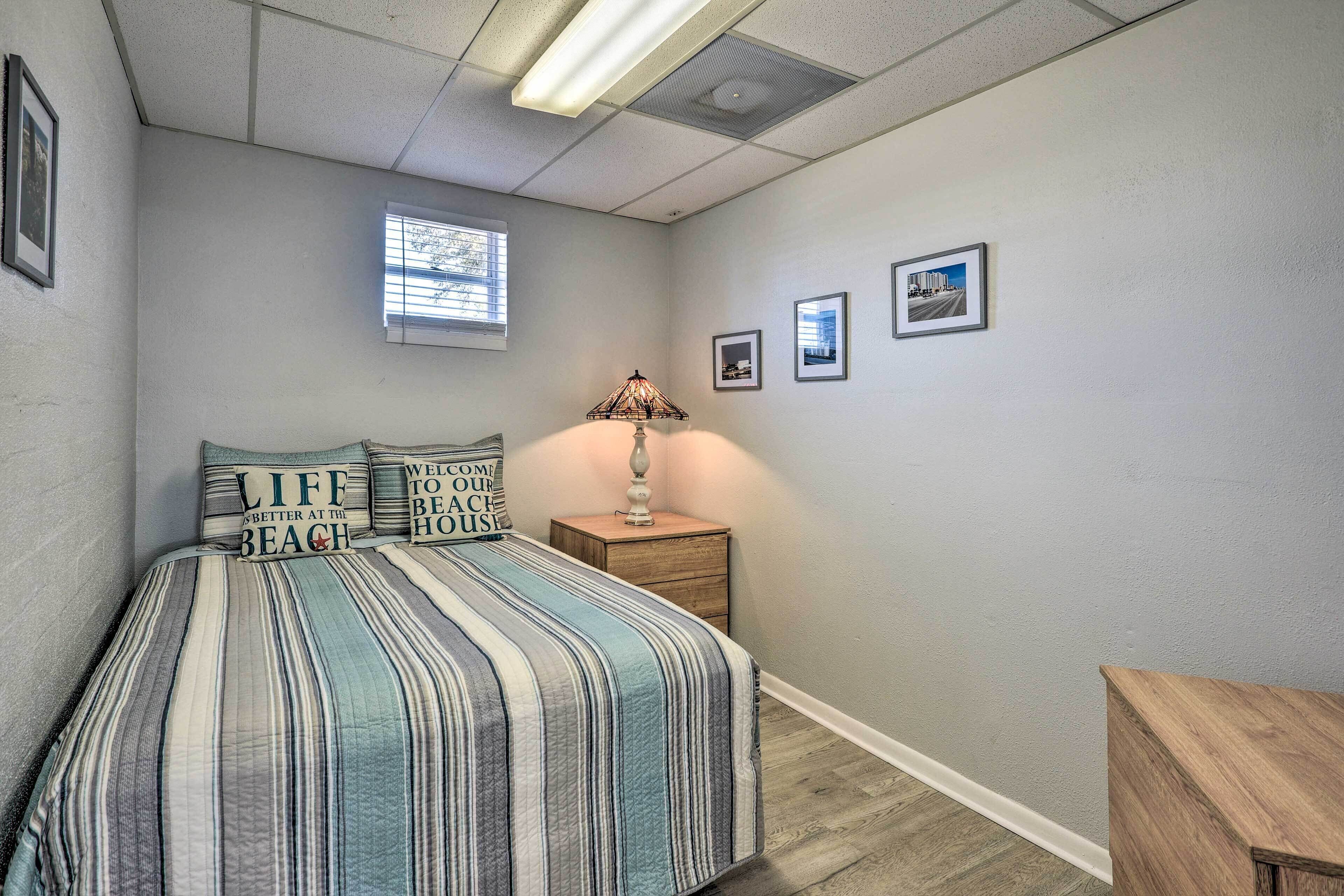 Un dormitorio con cama, mesita de noche, lámpara, ventana y cuadros en la pared.