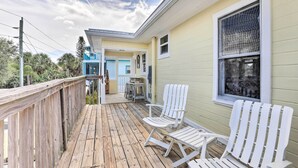 A wooden deck with two white Adirondack chairs, a covered patio area, and a yellow building with a large window. - Siesta Key Village Home < Half Mi to Beach! (Siesta Key)