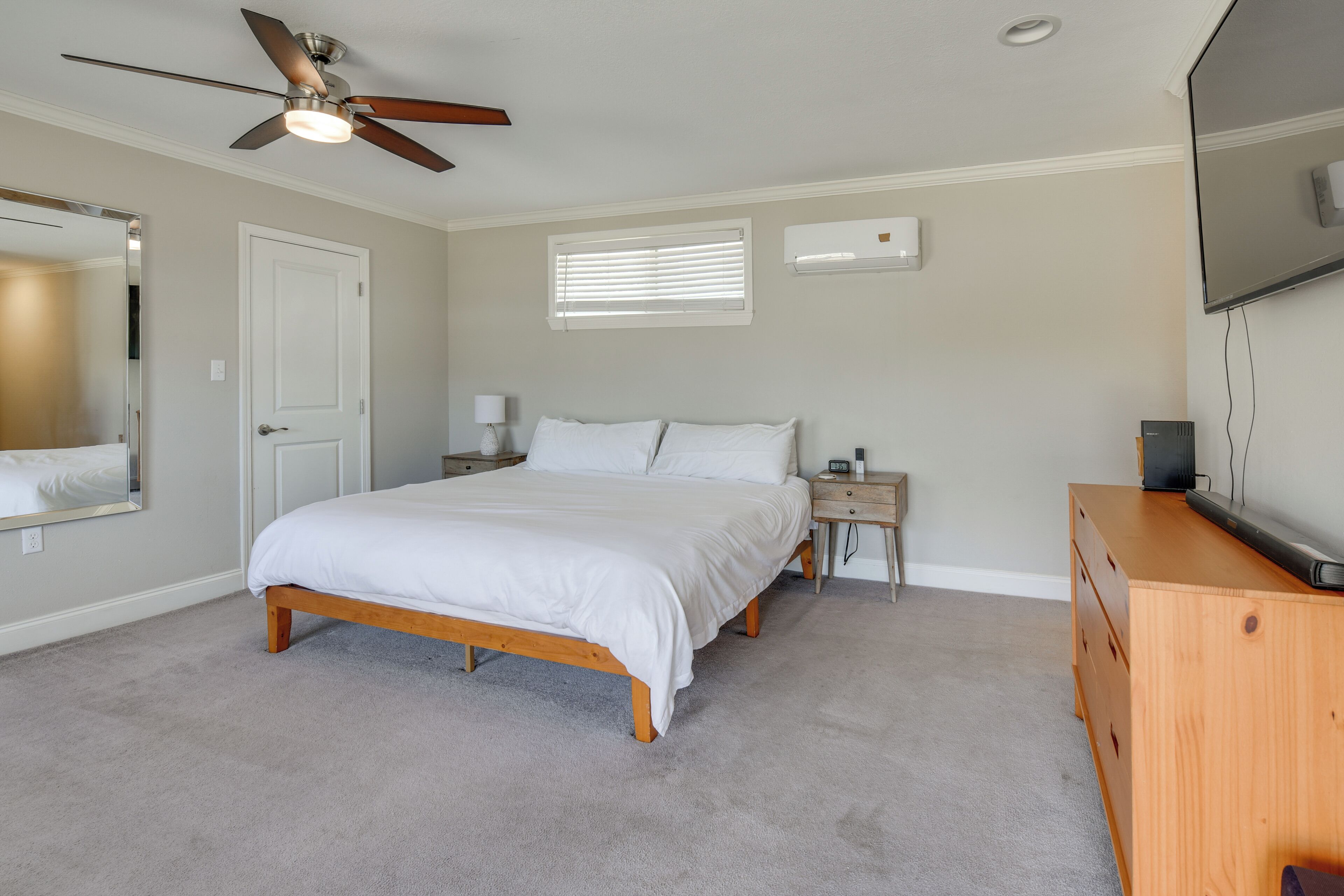 Een slaapkamer met een bed, nachtkastjes, een dressoir, een plafondventilator, een televisie, een raam met jaloezieën en een airconditioning.