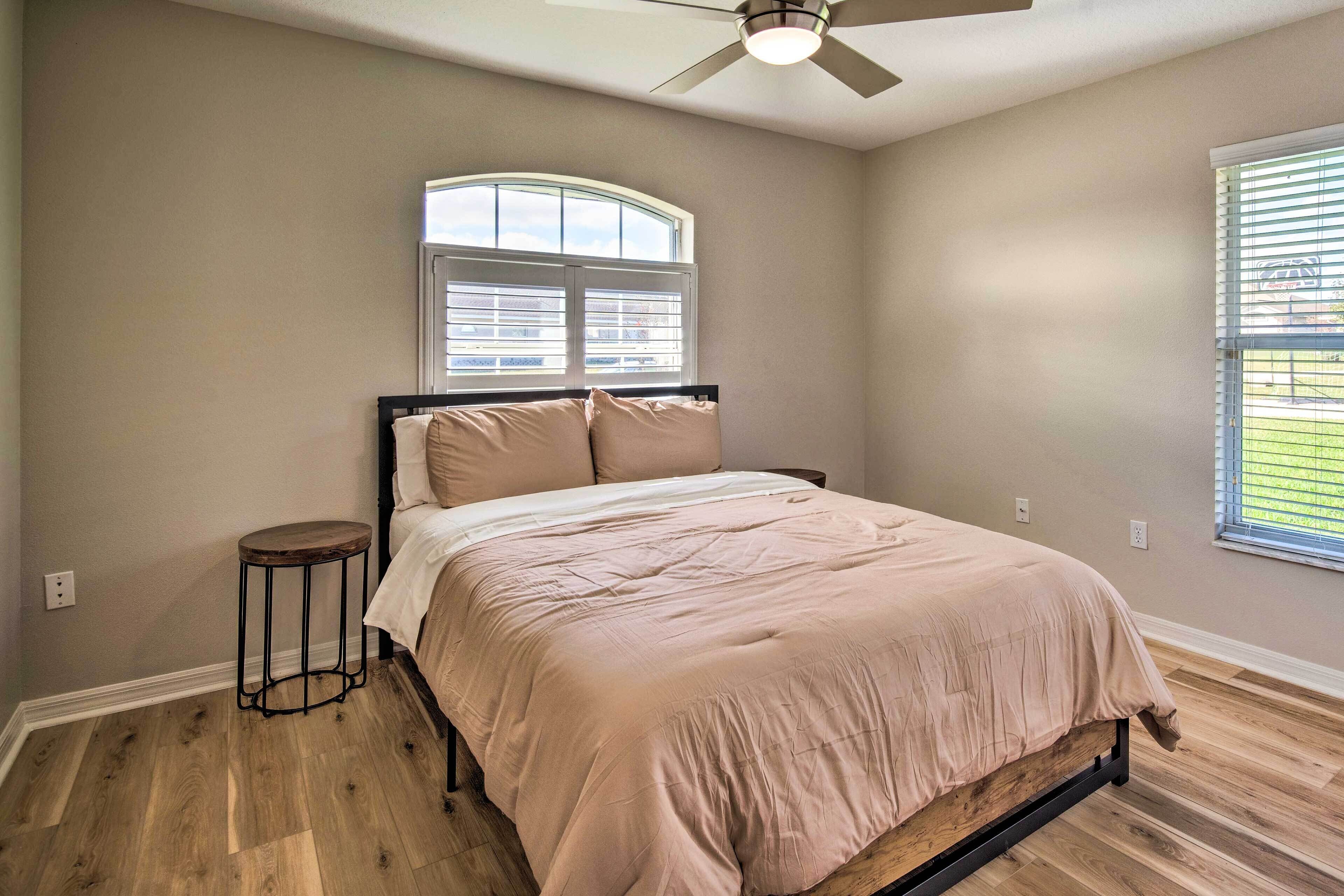 A bedroom with a bed, a standing lamp, a window, and a ceiling fan.