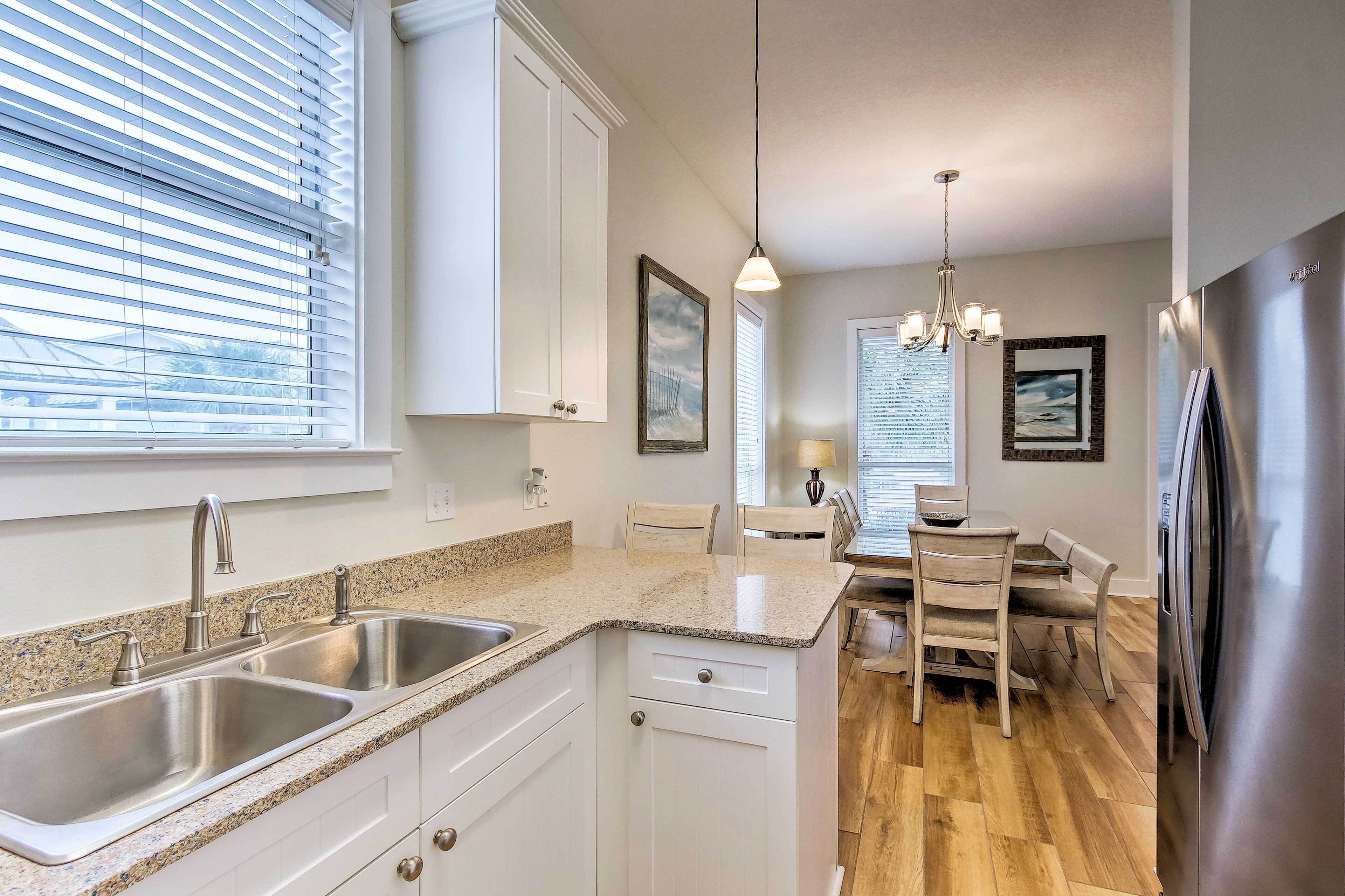 A modern kitchen with granite countertops, stainless steel appliances, and a dining area with wooden chairs.