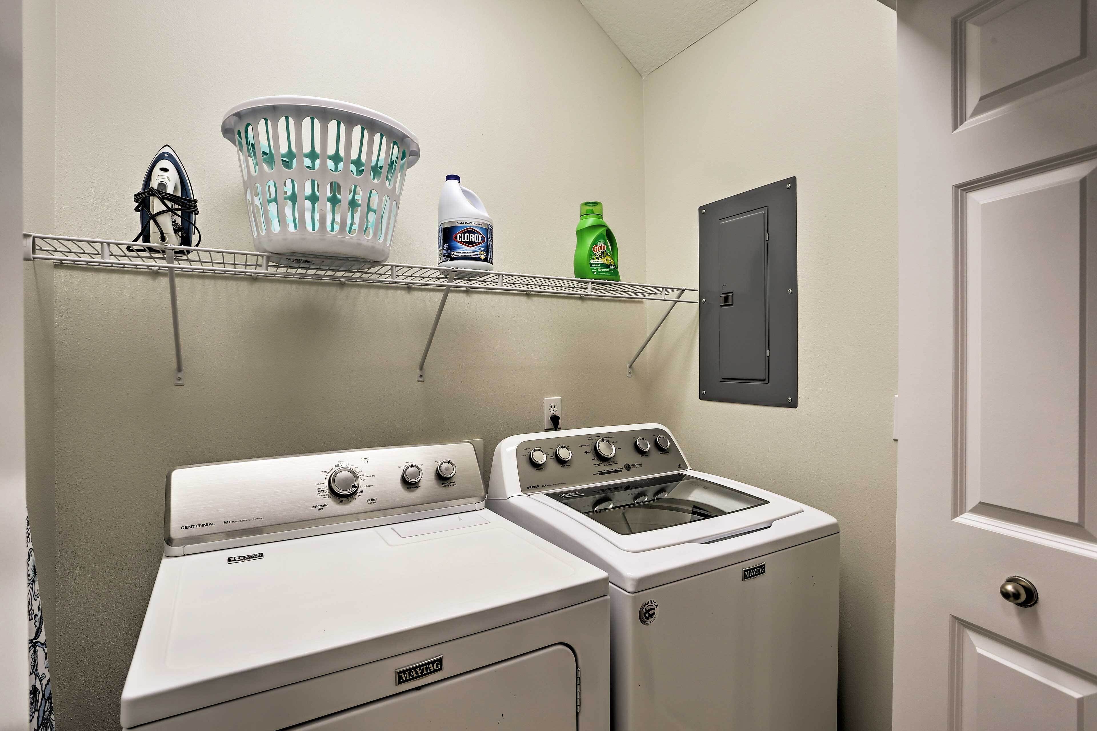 A laundry area with a Maytag washer and dryer, a basket, and detergent bottles on a shelf.
