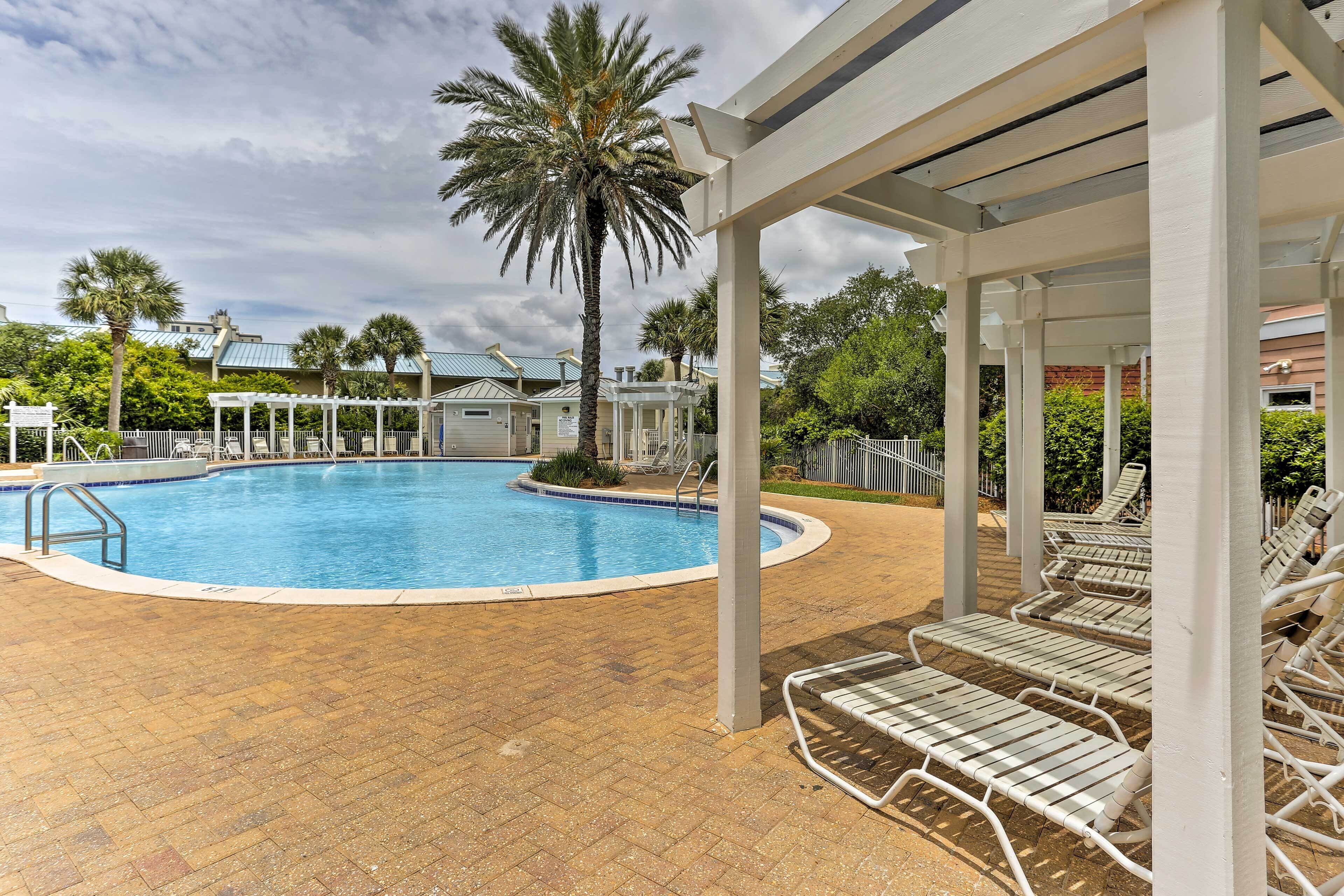 A pool area with lounge chairs, a covered seating area, and palm trees.