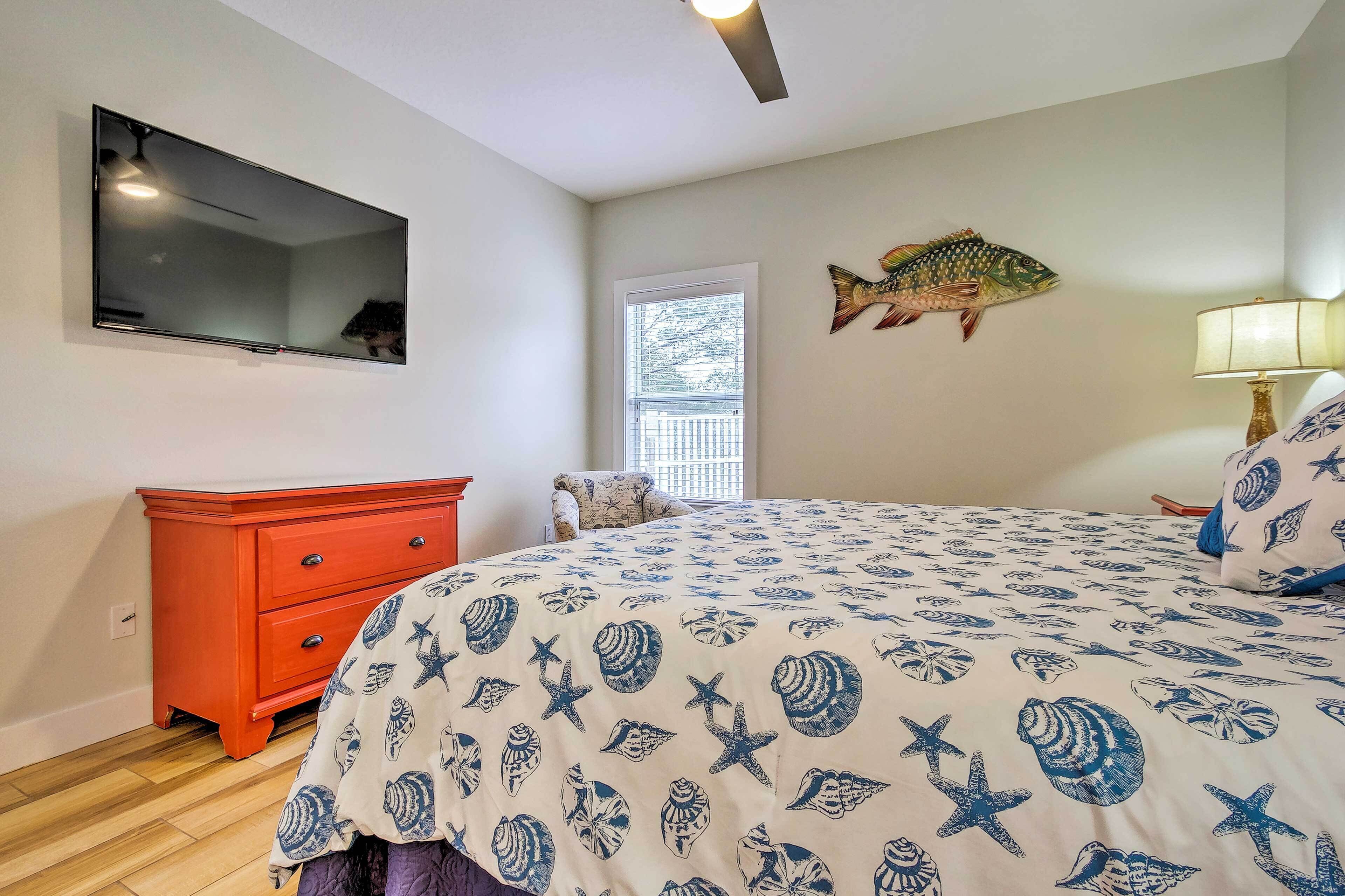 Een slaapkamer met een bed, een rode ladekast, een flatscreen-tv, een decoratie van een vis en een raam.