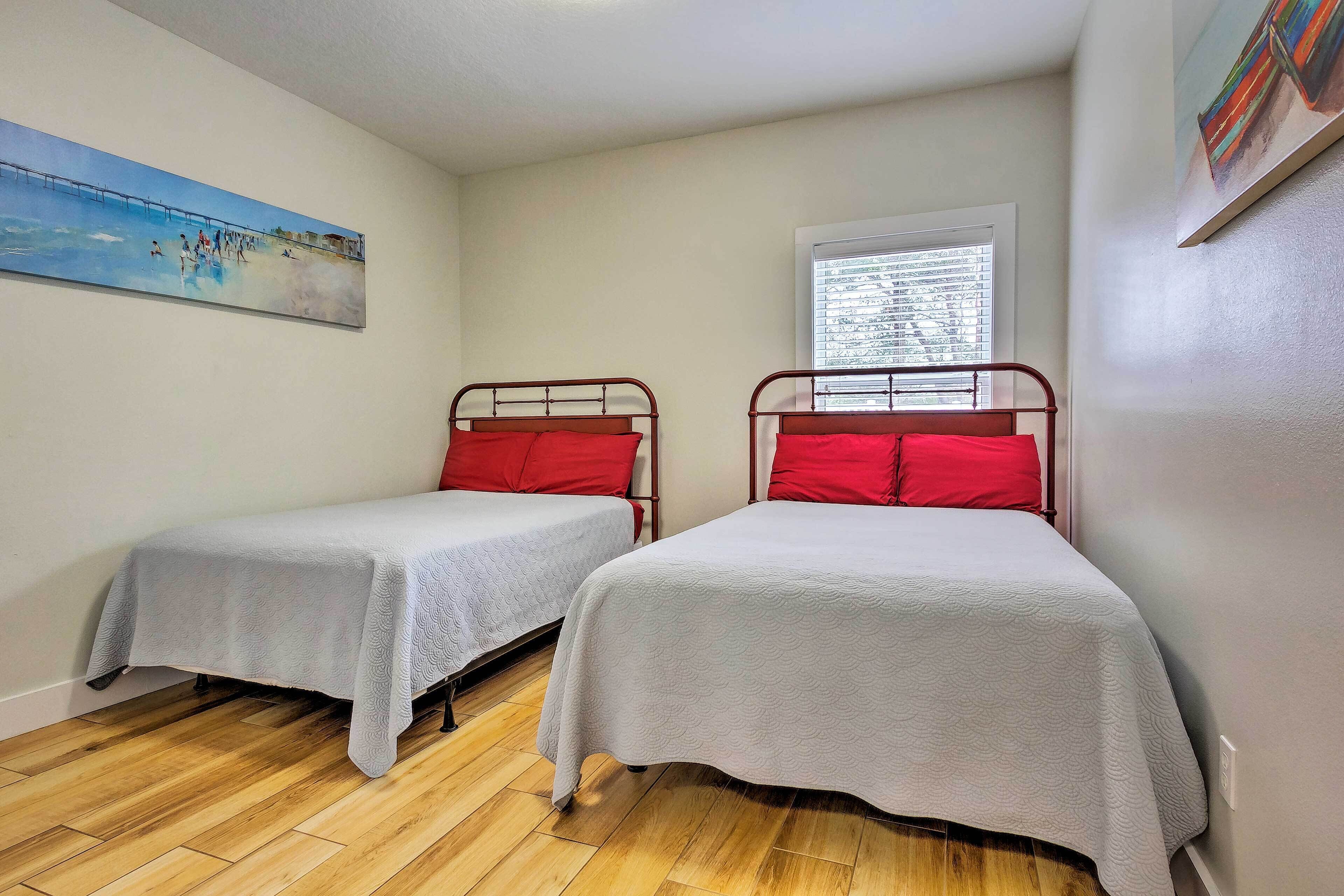 A bedroom with two single beds, a window with blinds, a painting on the wall, and a wooden floor.