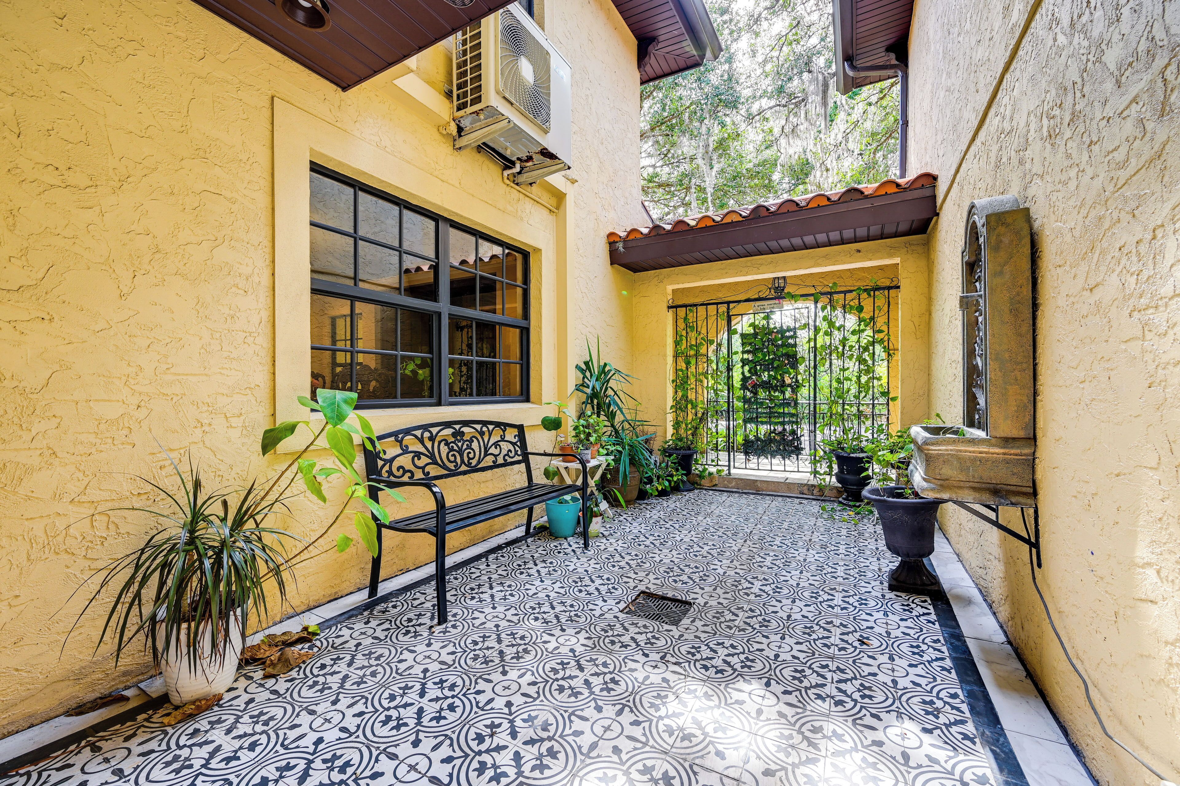 A courtyard with a tiled floor, a bench, potted plants, and a window.
