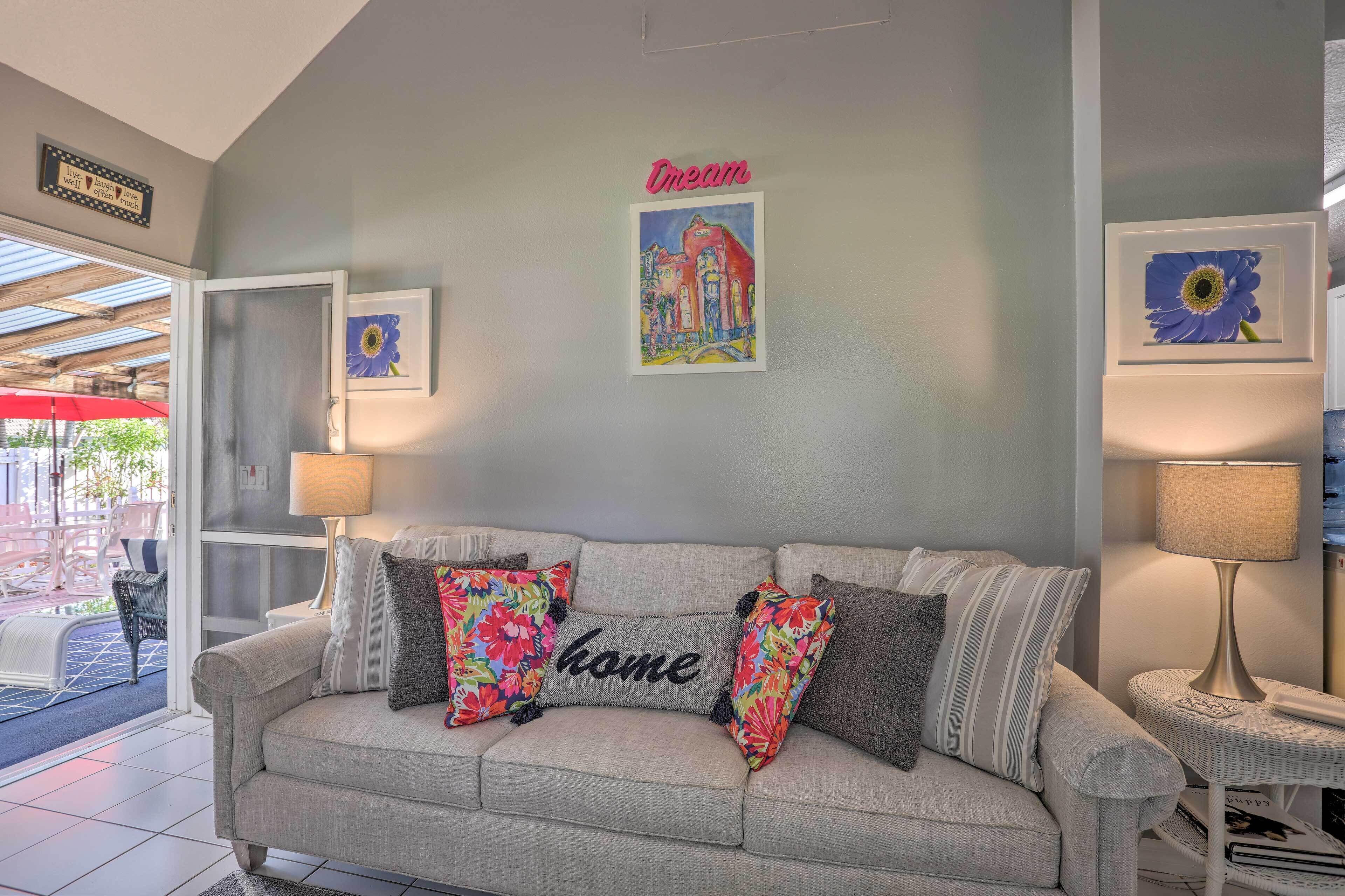 A living room with a grey sofa, colorful pillows, a framed picture of a building, and a 'Dream' sign.