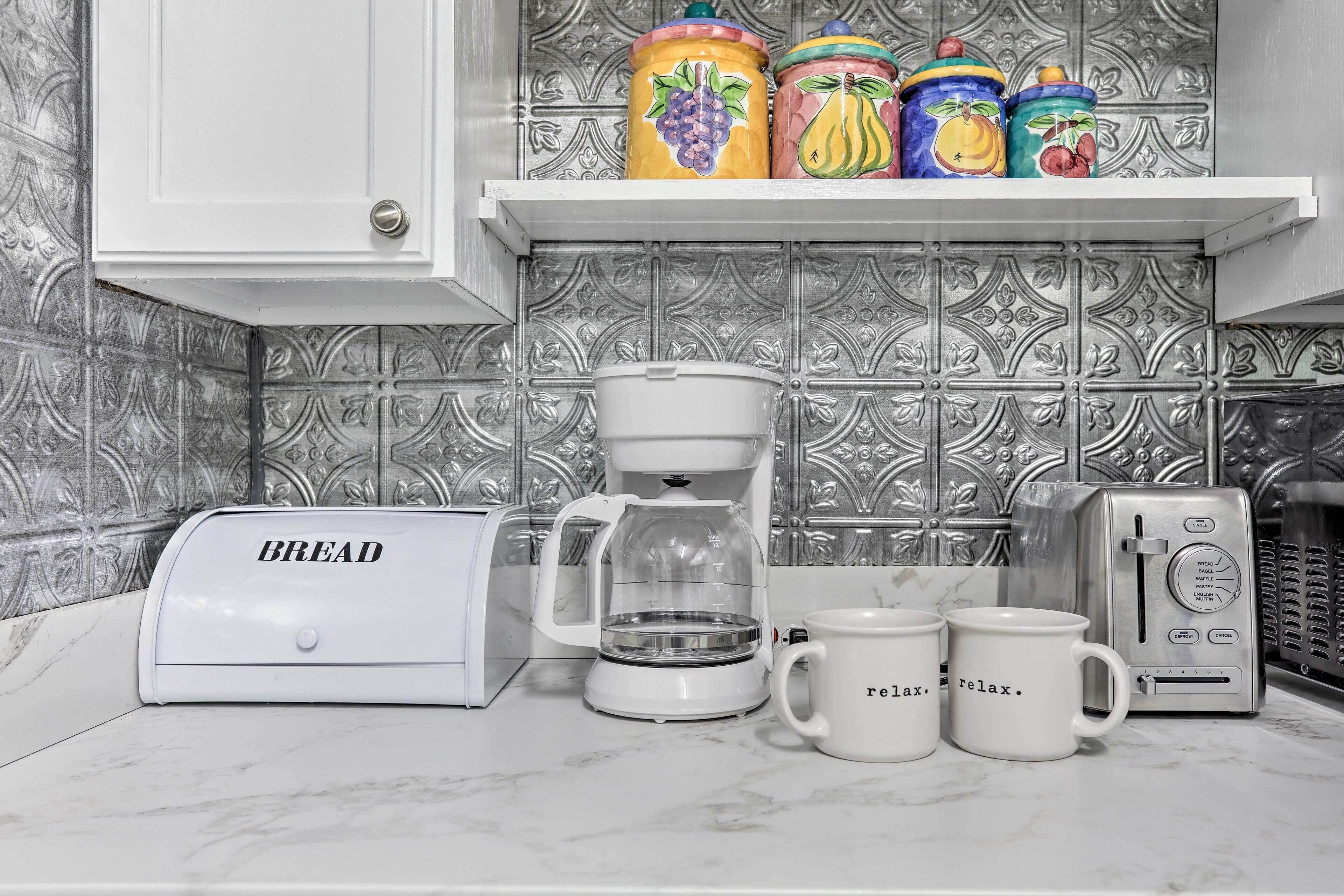 A kitchen with a bread maker, a coffee maker, and two mugs with the word 'relax.'