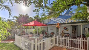 A covered patio with outdoor seating, a white picket fence, and tropical plants. - Stuart Apartment w/ Patio Near St Lucie River! (Stuart)