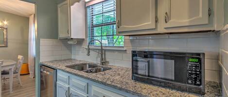A kitchen with white cabinets, a granite countertop, a built-in microwave, and a window with blinds.