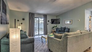 A living room with a grey sofa, a coffee table, and a lamp. There is a TV mounted on the wall and a window with curtains. - Stellar Fort Walton Retreat ~ 2 Mi to Beach! (Fort Walton Beach)