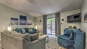 A modern living room with a grey sofa, a blue armchair, and a flat-screen TV mounted on the wall. - Stellar Fort Walton Retreat ~ 2 Mi to Beach! (Fort Walton Beach)