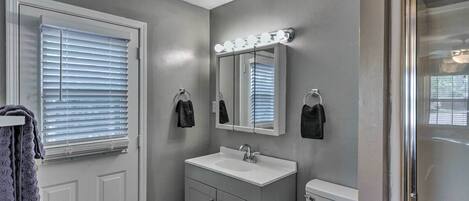 A bathroom with a vanity, sink, mirror, and toilet.