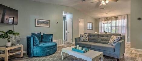 A living room with a teal sofa, a grey sofa, a white coffee table, and a ceiling fan.