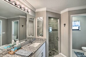 Un baño con encimera de granito, cabina de ducha con mampara de vidrio y tocador con espejo.