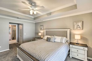 Un dormitorio con cama, mesitas de noche, ventilador de techo y obras de arte en las paredes.