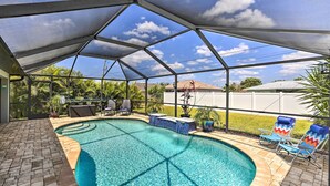 A covered outdoor swimming pool with a brick border, lounge chairs, and potted plants. - Stunning Cape Coral Home w/ Open Floor Plan! (Cape Coral)