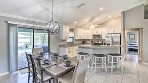 A modern kitchen with white cabinets, a central island, and a dining area with a large table and chairs. - Stunning Cape Coral Home w/ Open Floor Plan! (Cape Coral)