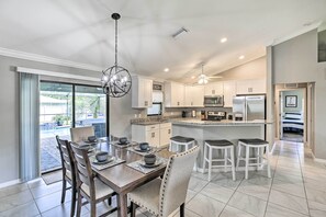 A modern kitchen with white cabinets, a central island, and a dining area with a large table and chairs. - Stunning Cape Coral Home w/ Open Floor Plan! (Cape Coral)