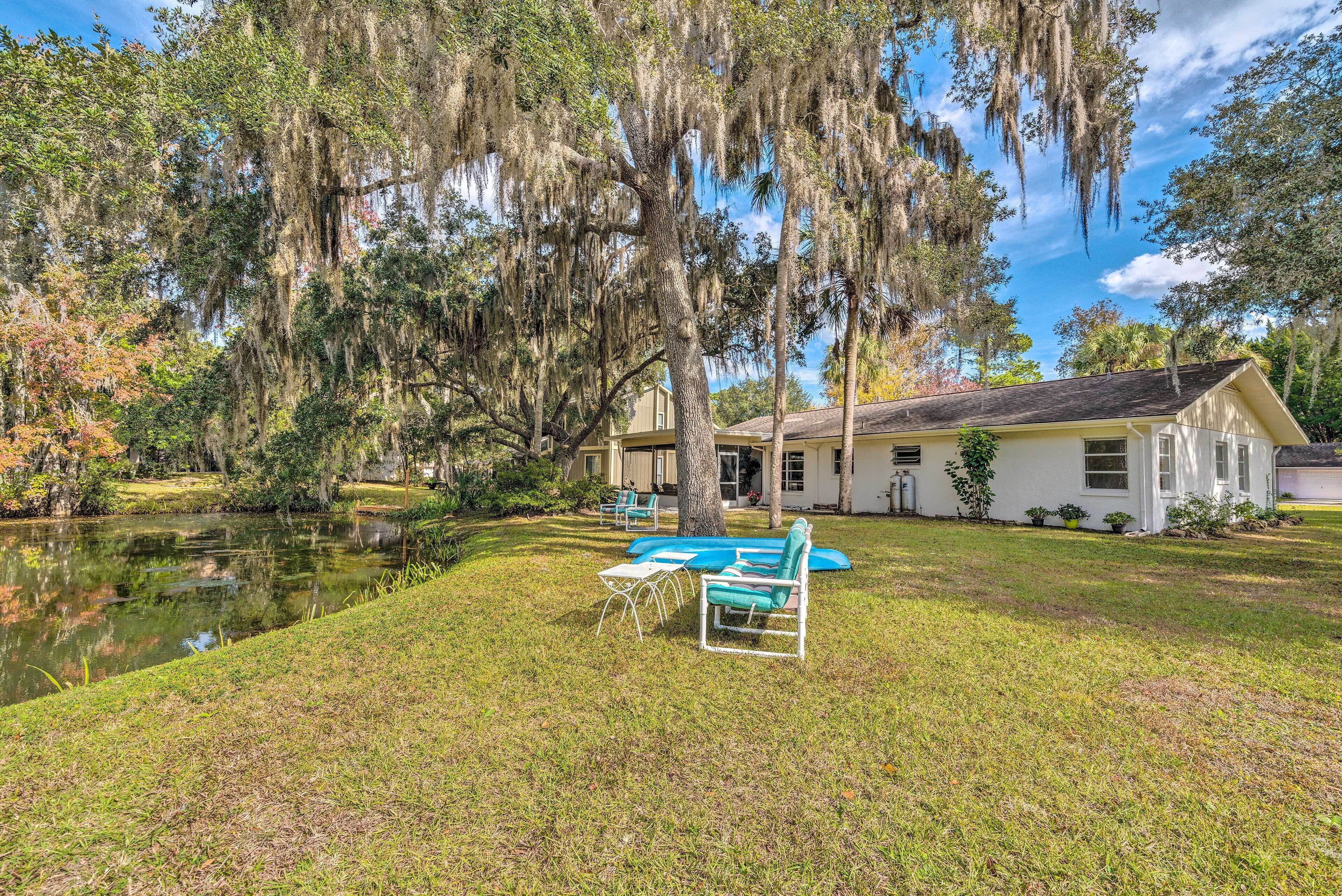 A house with a pond, surrounded by trees with Spanish moss, and outdoor furniture.