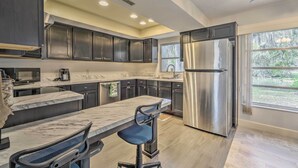 A modern kitchen with dark cabinets, a stainless steel refrigerator, a marble countertop, and a bar stool. - Sunny Crystal River Home w/ Screened-in Porch (Crystal River)