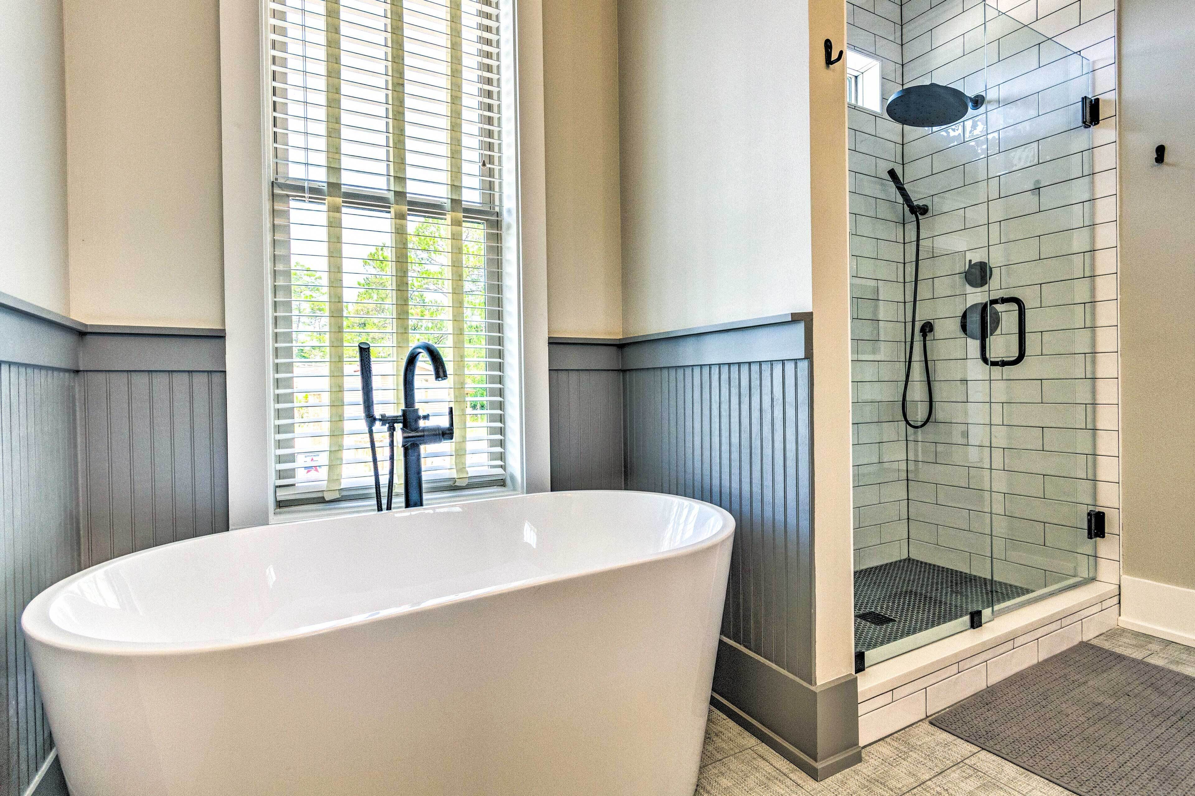 Un baño moderno con una bañera independiente, una ducha con cerramiento de vidrio y una ventana con persianas.