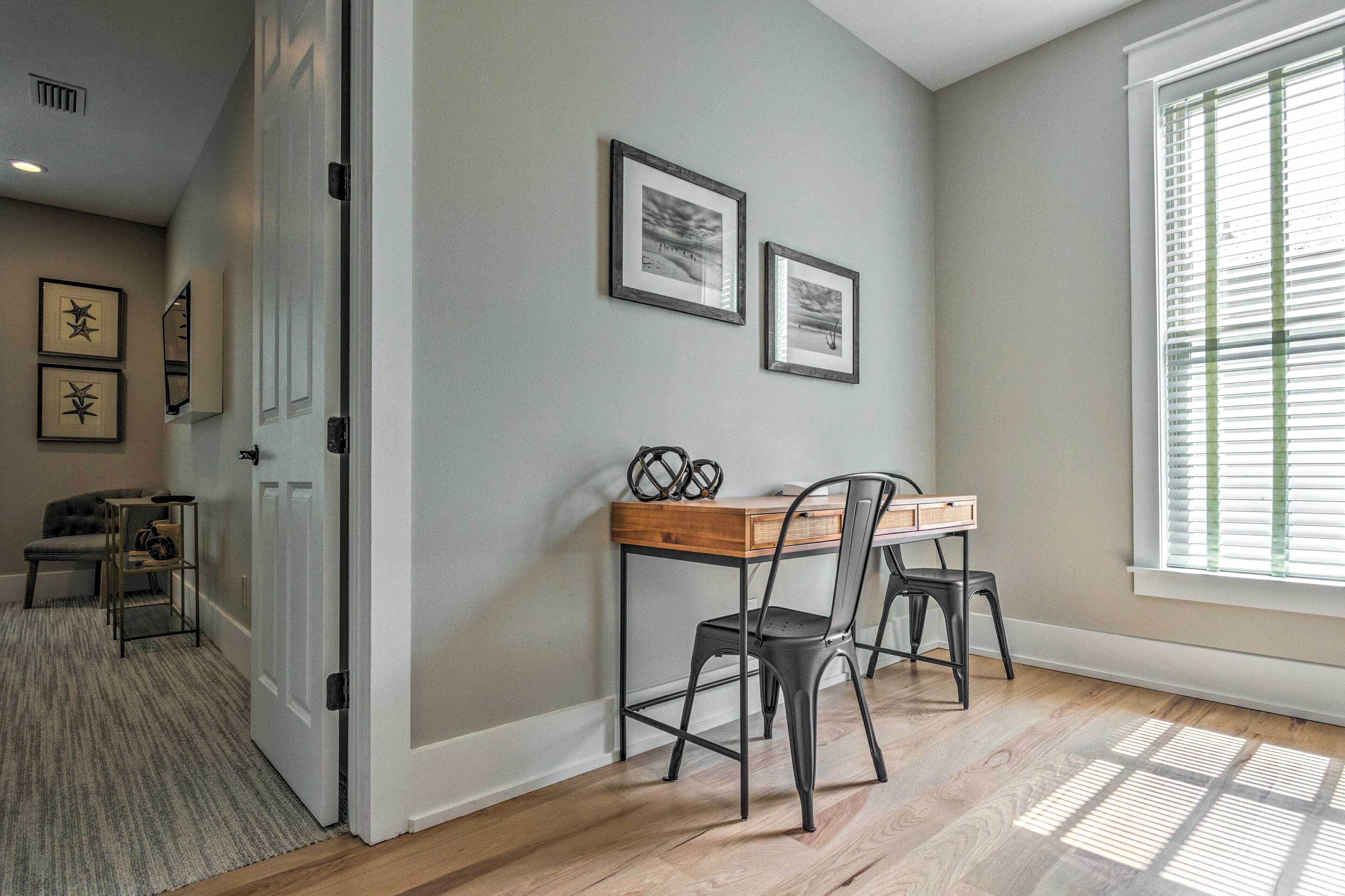 A room with a wooden desk, two chairs, and framed pictures on the wall.