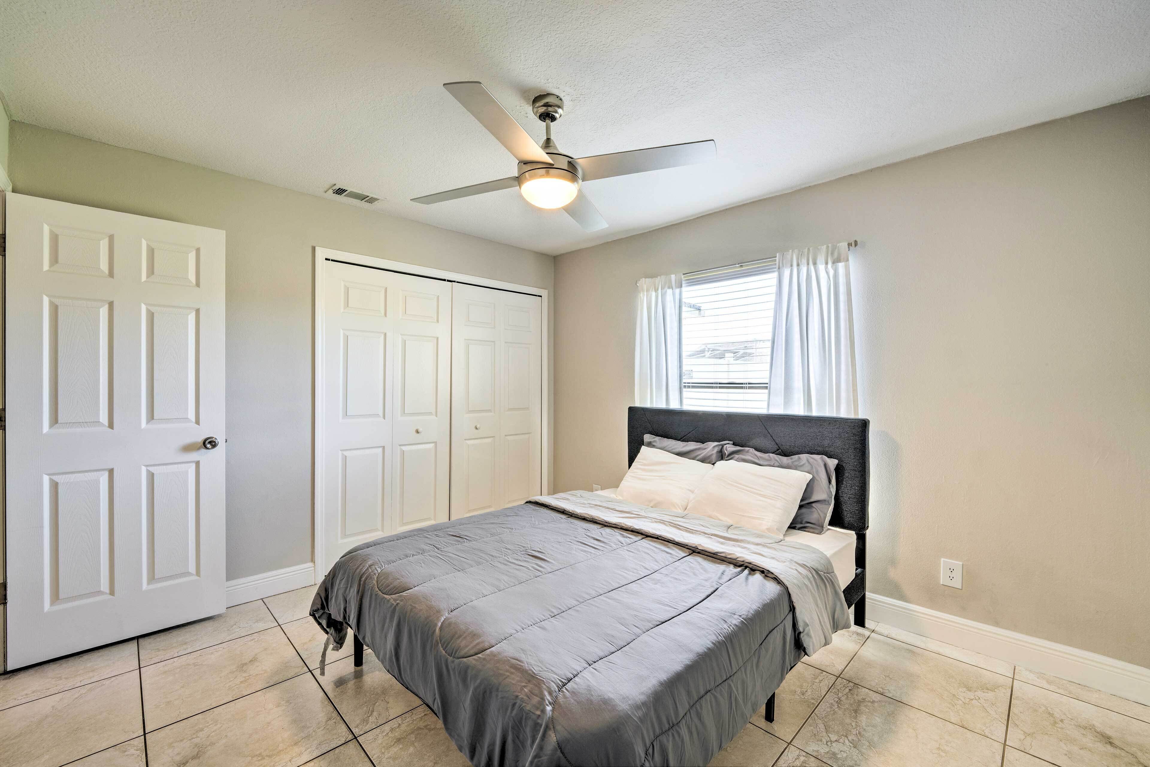 A bedroom with a bed, a ceiling fan, a window with curtains, and a door.