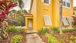 A yellow building with a concrete pathway leading to a door, surrounded by various plants and shrubs. - Kissimmee Resort Townhome w/ Pool, 7 Mi to Disney! (Kissimmee)
