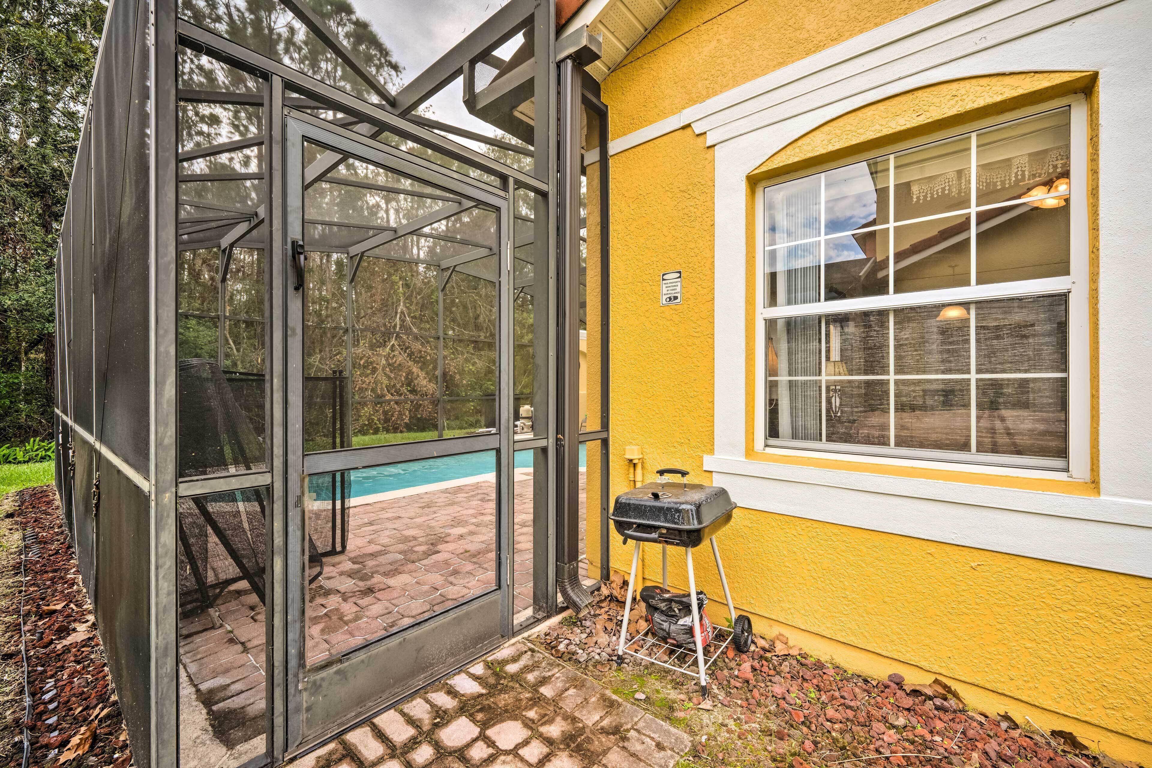 A glass-enclosed patio with a barbecue grill, a pool, and a yellow building.