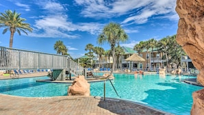 A swimming pool with clear blue water, surrounded by palm trees and a rocky landscape. - On-site Beach Bar: Sunny Perdido Key Cottage! (Pensacola)