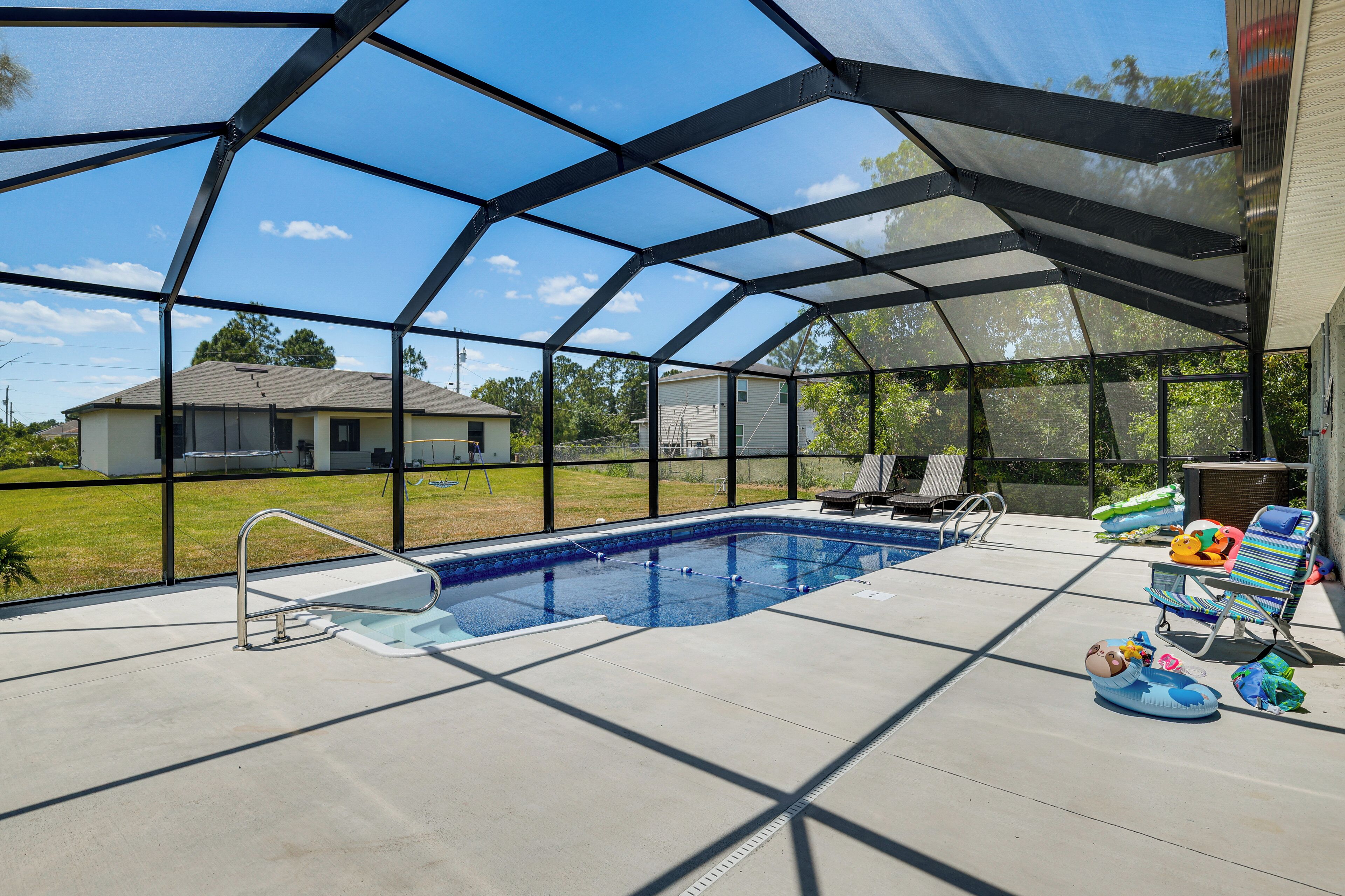 Una piscina exterior techada con vistas despejadas al jardín, una escalera de piscina y sillas de descanso.