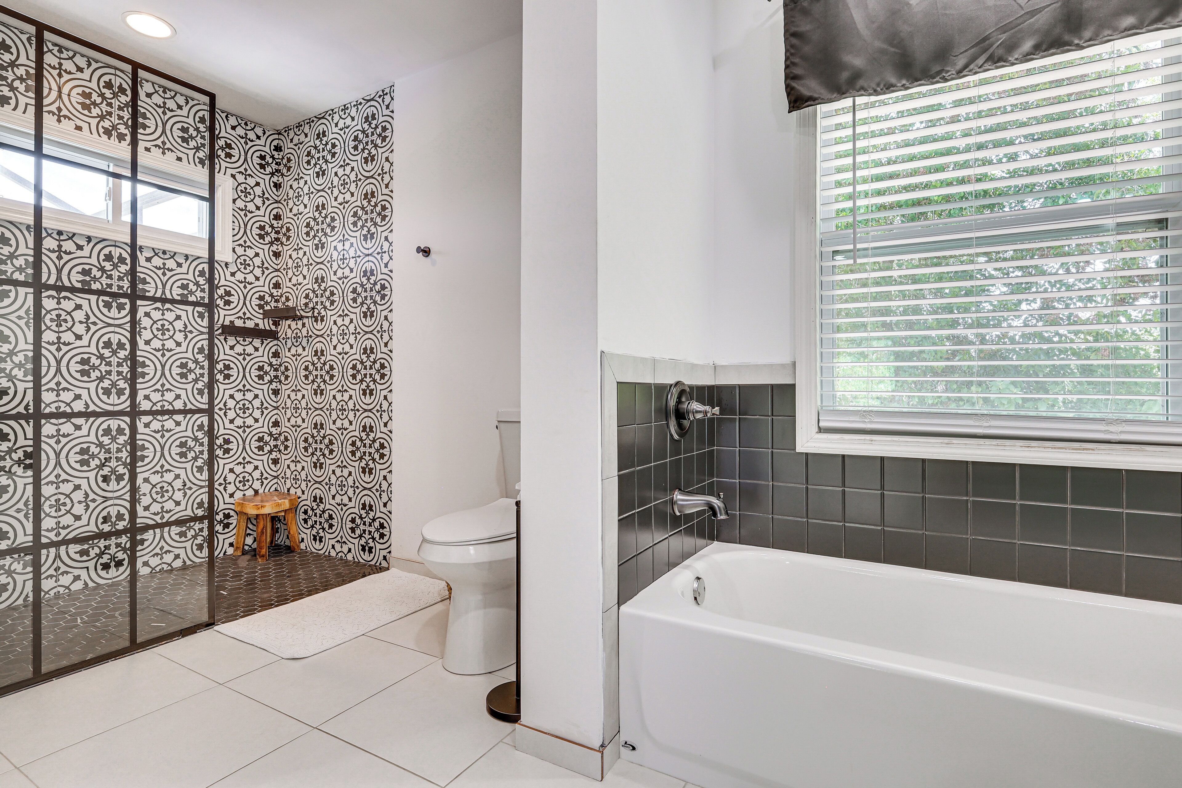 Un baño con bañera, inodoro, zona de ducha y ventana con persianas.