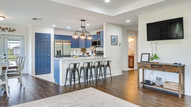 A spacious living area with a kitchen island, bar stools, a large TV, and a wooden console table.