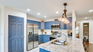 A modern kitchen with blue cabinets, stainless steel appliances, and a granite island.