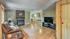 Ein Wohnzimmer mit Ledersofa, Flachbildfernseher, Kamin und Essbereich im Hintergrund.