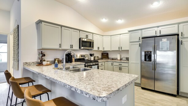 Una cocina moderna con armarios blancos, un refrigerador de acero inoxidable, una encimera de granito y una zona con taburetes de bar.