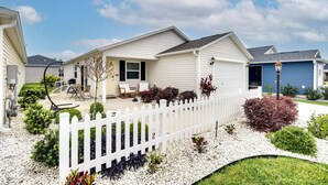 Una casa residencial con cerca de piquetes blancos, un patio con mobiliario exterior y un jardín bien cuidado.