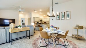 Una sala de estar moderna con un sofá, televisor y una zona de comedor con sillas y una mesa.