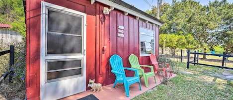 A red building with a large sliding glass door, two Adirondack chairs, and a small dog on the porch.